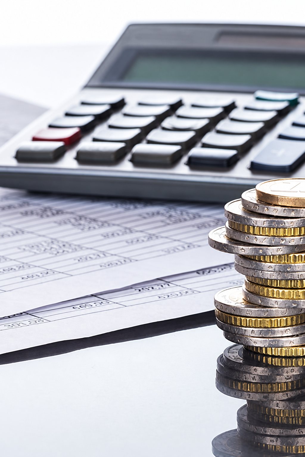 Pile de pièces d’euro devant une calculatrice et des documents comptables